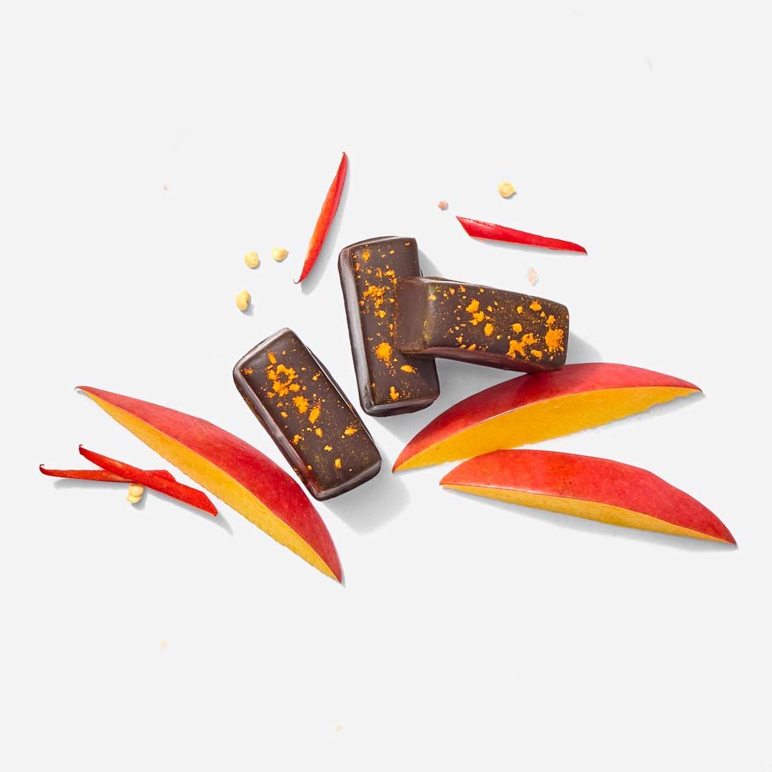 Signature Caramel Gift Box three dark chocolate bars speckled with orange zest beside mango slices on a white background