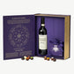 A large purple giftbox sits open revealing a bottle of Ceretto wine and a chocolate box tied with purple ribbon surrounded by several chocolate truffles on a grey background.