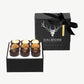 Nine Vosges Dalmore chocolate truffles topped with spiced ginger crumble, gold leaf and candied orange peel sit in a open, black candy box adorned in silver foil tied with a black ribbon bow on a white background.