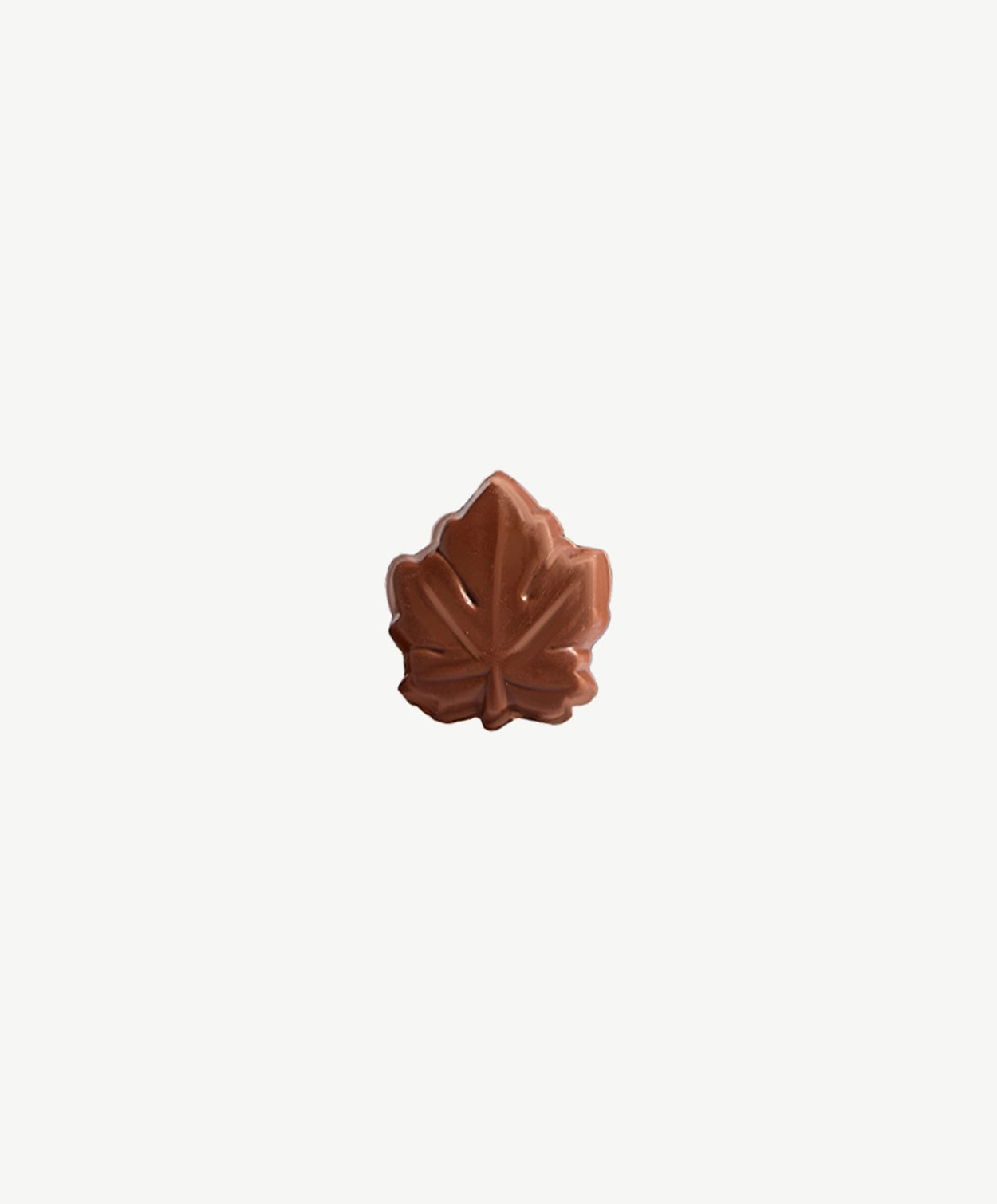 A close up of a Vosges Chocolate Maple Bomba Bite on a light grey background.