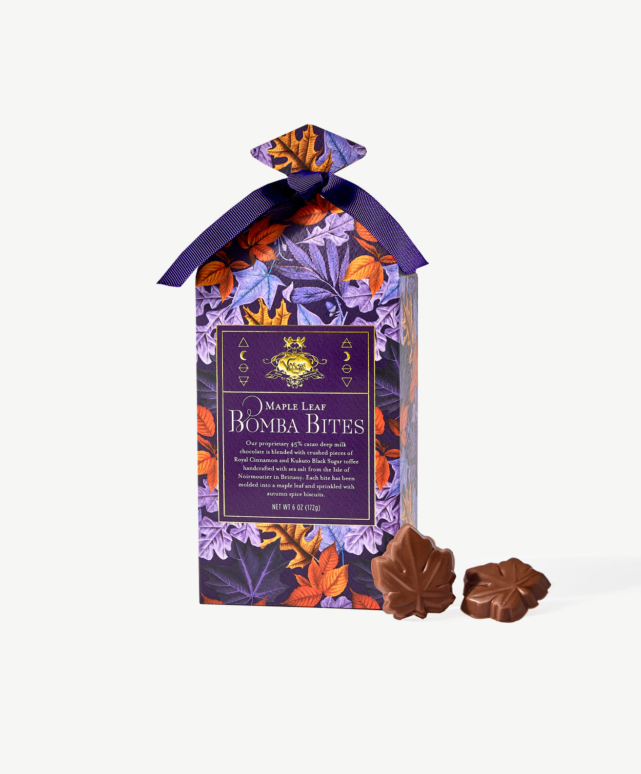 A tall gable box decorated in purple and autumn colored leaves, tied with a purple ribbon stands beside two small chocolate maples leaves on a light grey background.