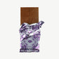 Unwrapped Vosges Mo's Milk Chocolate Bacon Bar in a silver wrapper stands upright on a white background.