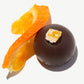 Close-up of a Vosges Sicilian Blood Orange vegan truffle next to a slice of fresh orange topped with a candied orange peel on a white background.