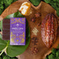 Vosges Chinese 5-Spice Bar on a large green leaf beside a cacao pod surrounded by green moss, honey comb and spices.