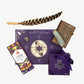 A Vosges truffle collection sits beside an ornately decorated notebook, a leather wrapped turkey feather, sage bundle, turmeric ginger bar and a meditation guide car on a white background.