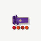 Four Vosges Vegan chocolate truffles adorned with vibrant red raspberry powder and orange powder sit infront a rectangular purple candy box embossed with gold foil tied with a purple ribbon bow on a grey background.