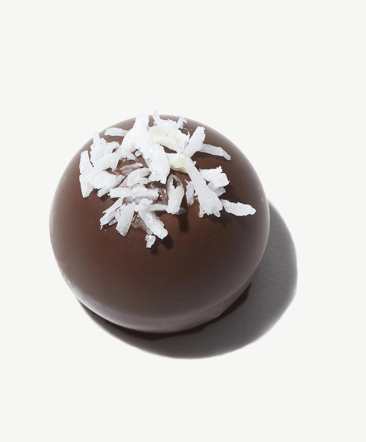 Close-up of a Vosges milk chocolate Wooloomooloo truffle topped with Sri Lankan coconut on a white background.