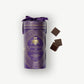 A tall purple tube embossed with the words, "Caramels et Chocolats" in gold foil, tied with a purple ribbon sit beside three chocolate covered caramels on a light grey background.