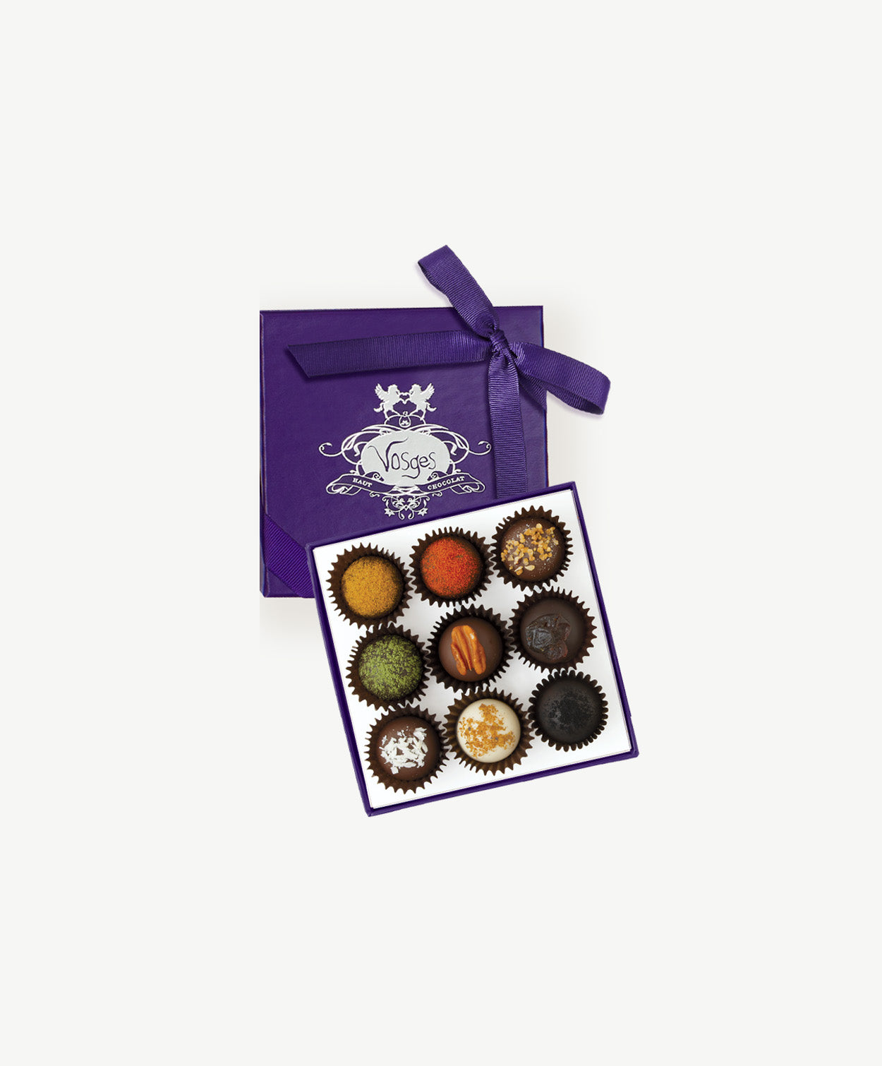 Open purple chocolate box of Vosges haut-chocolat exotic truffles adorned in brightly colored spices and toppings tied with a purple ribbon bow on a white background.