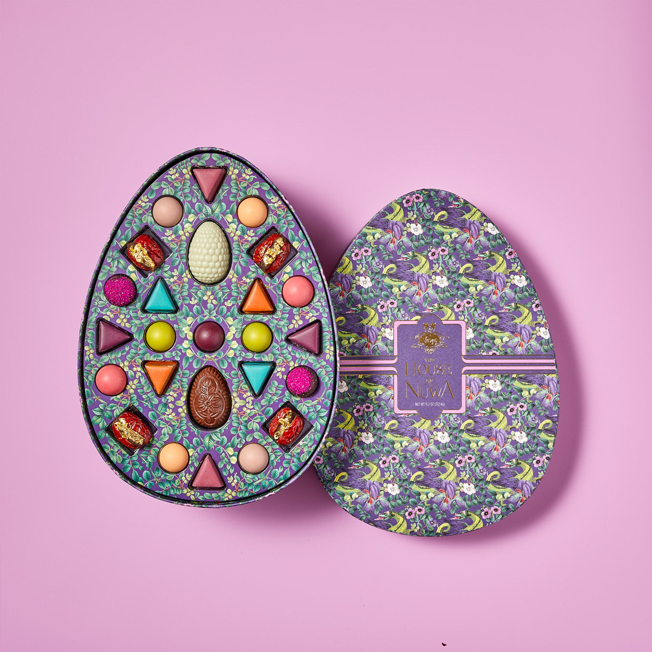 An opened purple and green chocolate box displaying twenty five unique, colorful Vosges truffles on a light purple background.