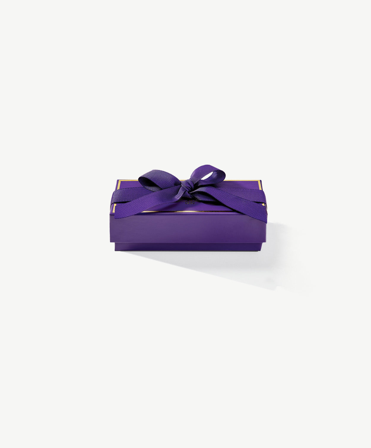 A small, rectangular purple chocolate candy box embossed with gold foil Vosges Haut-Chocolat logo sits closed on a grey background.