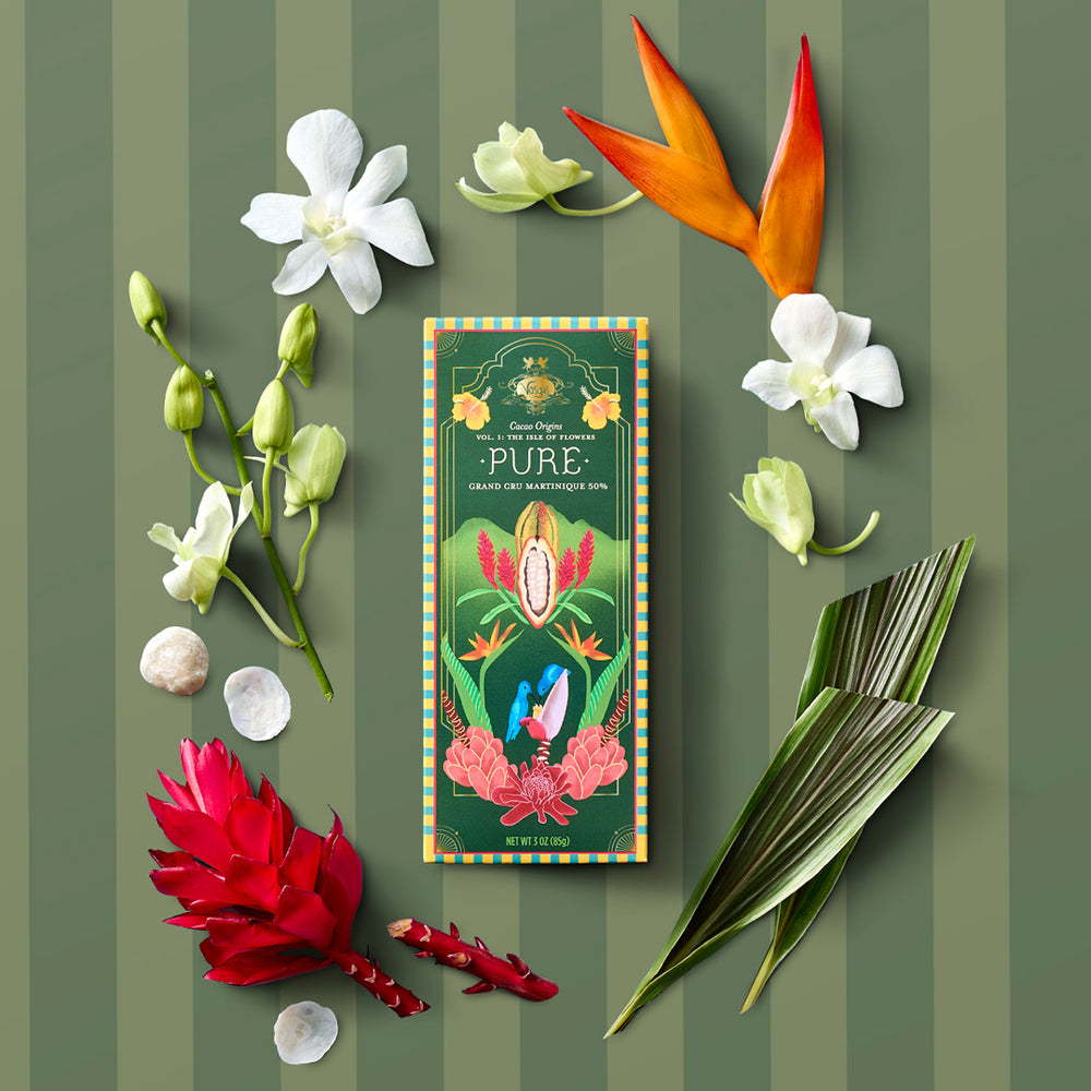 Pure single-origin Martinique chocolate bar on a green backdrop surrounded by tropical flowers and leaves.