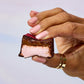 Close-up of a pink raspberry caramel marshmallow bite held between fingers showing pink center and chocolate coating.