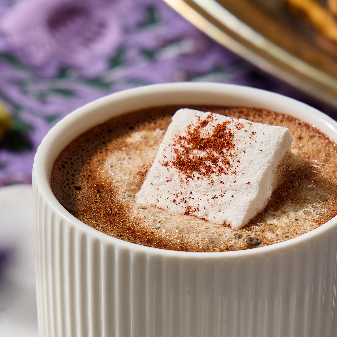 White mug with hot chocolate and a marshmallow garnished with cinnamon, blurred floral background