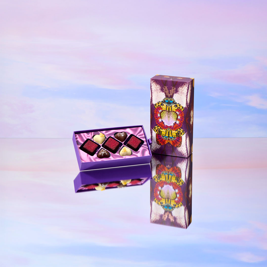 Purple chocolate box with truffles on a reflective surface with a colorful gradient background