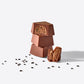 Three stacked milk chocolate blocks with a crumbly interior exposed and coffee beans scattered around.