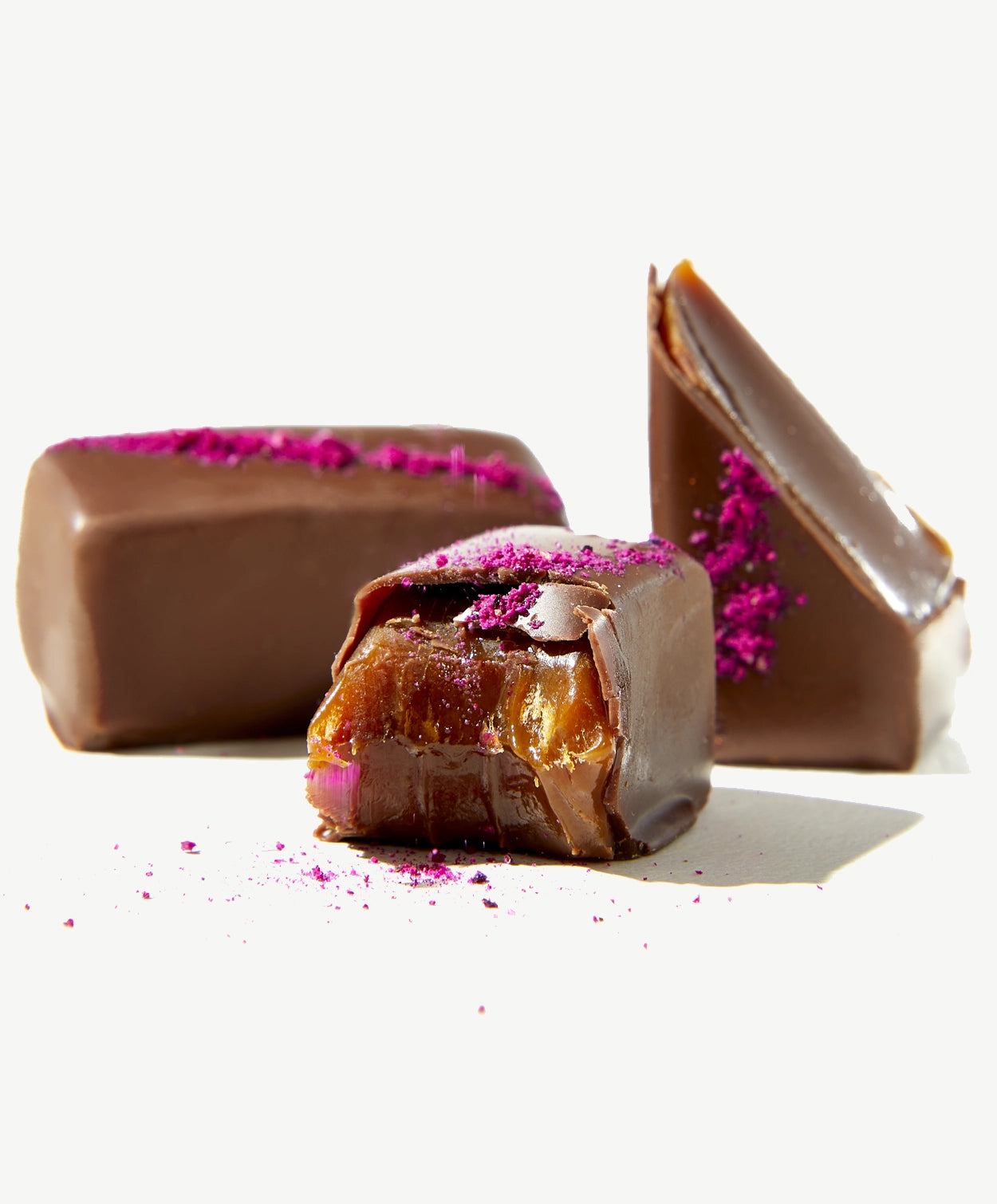 Close up of two Vosges caramels, one bitten displaying buttery caramel center and milk chocolate coating on a white background.