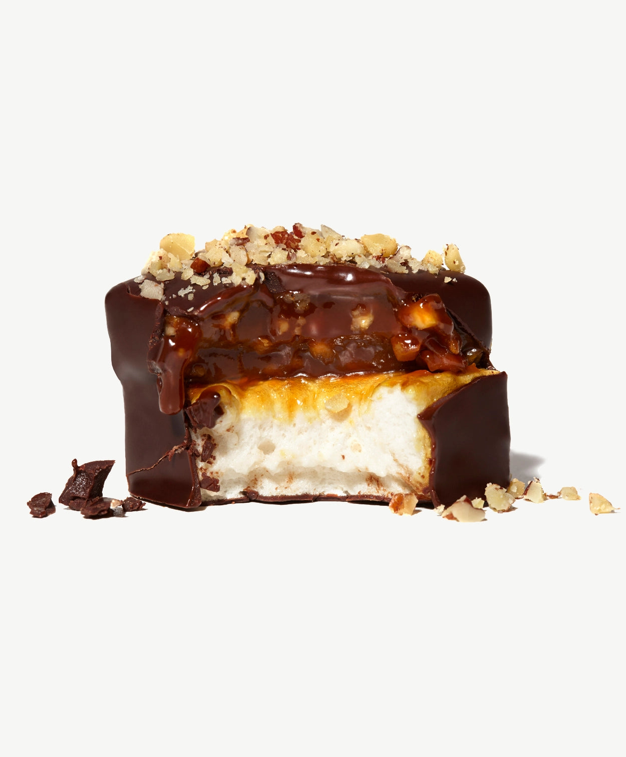 Close-up of a Vosges Caramel Marshmallow with a bite taken showing layers of Caramel, Marshmallow chopped walnuts and pecans on a white background.