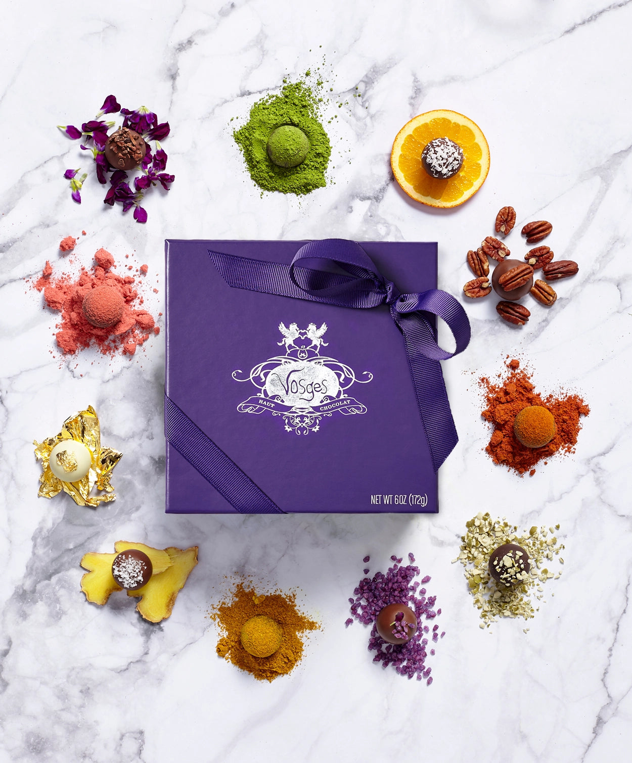 Purple Vosges Haut-Chocolat chocolate box tied with ribbon surrounded by fresh ingredients and exotic truffles on a marble slab.