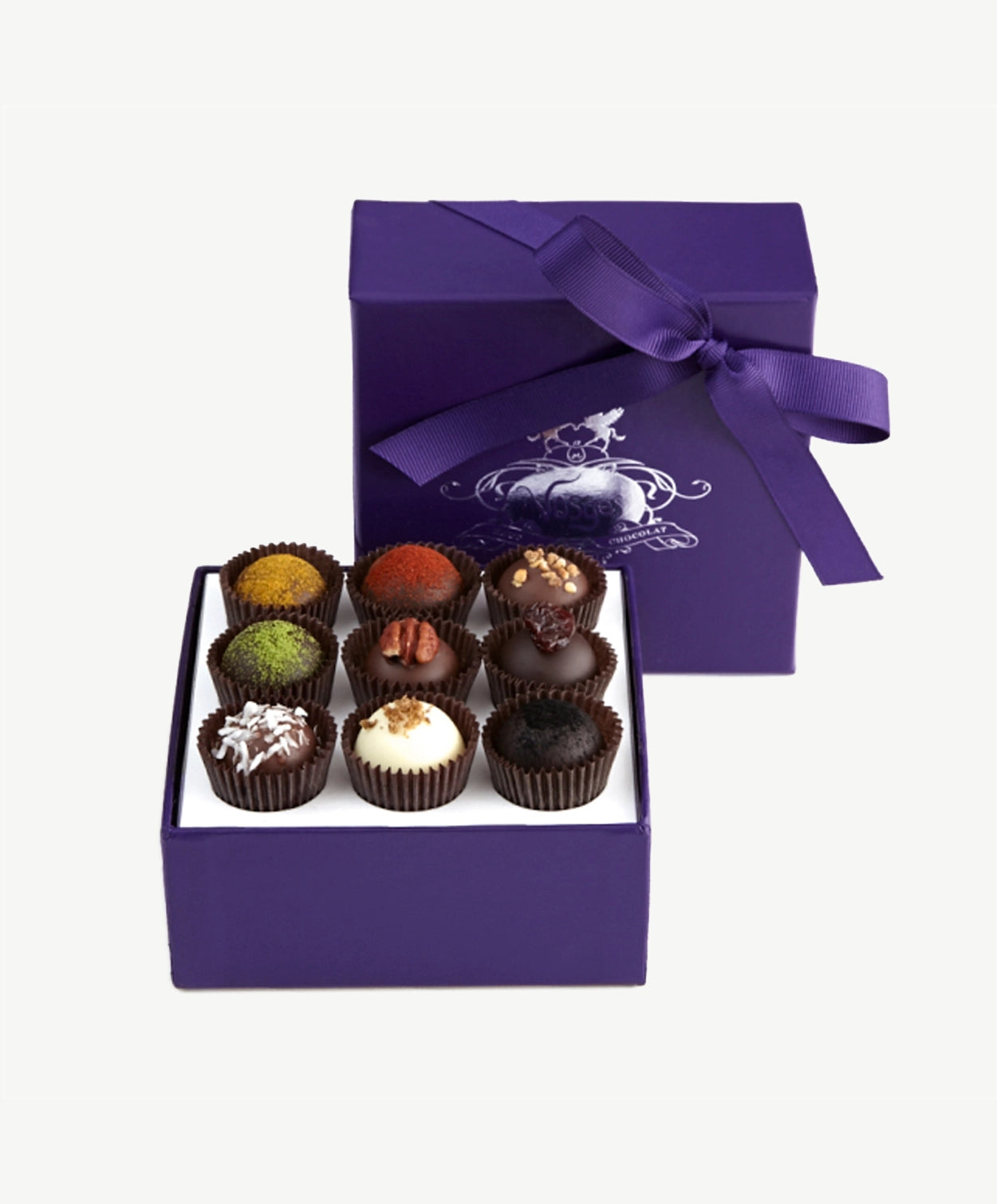 Purple box of Vosges haut-chocolat exotic truffles, lid standing upright, displaying nine chocolate truffles adorned in brightly colored spices and toppings tied with a purple ribbon bow on a white background.