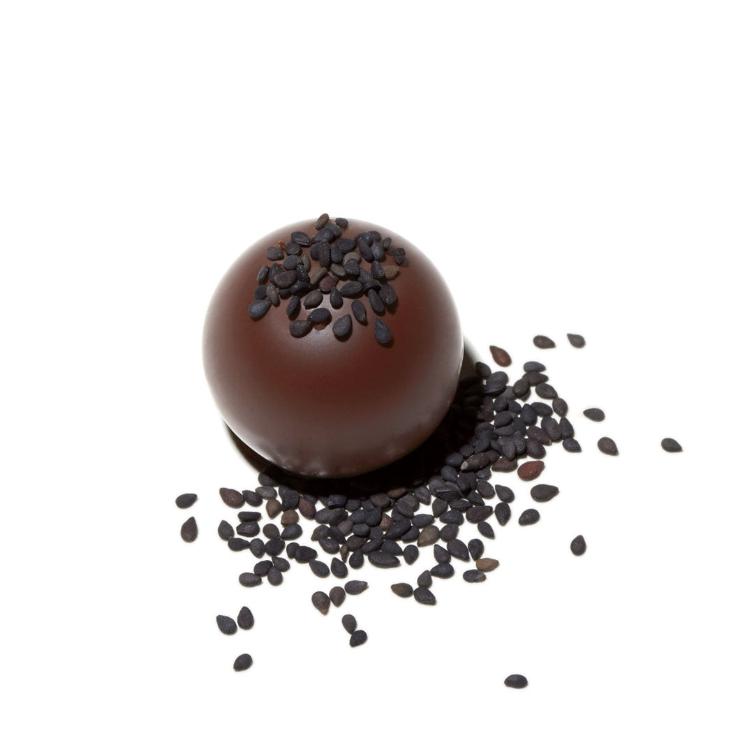 Glossy dark chocolate truffle topped with black sesame seeds on a white background