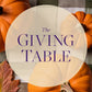 The Giving Table title centered on a translucent circle over a pumpkin backdrop.