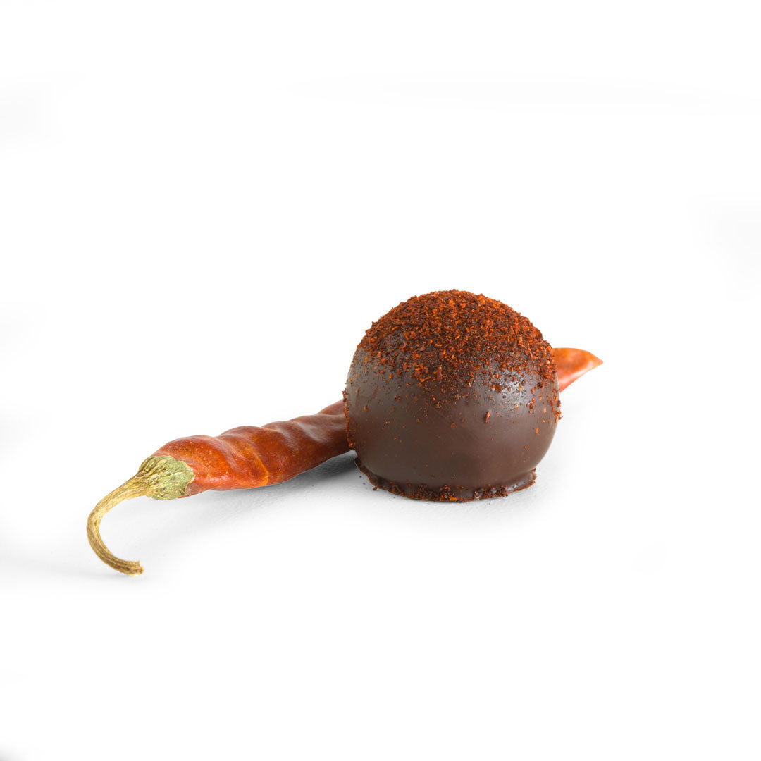 Red Fire Truffles chocolate ball coated in red chili flakes with a dried red chili beside it on a white background