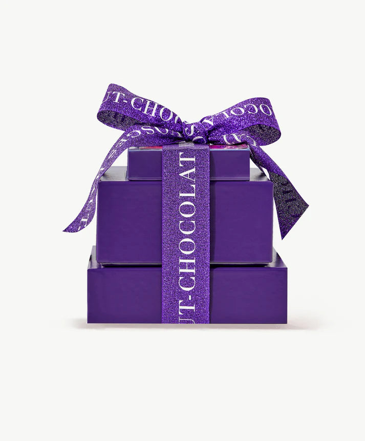 Three purple Vosges chocolate boxes sit in a tower tied with a thick purple ribbon bow on a white background.