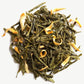 A close up of dark green Alizes Wind Tea leaves on a light grey background.