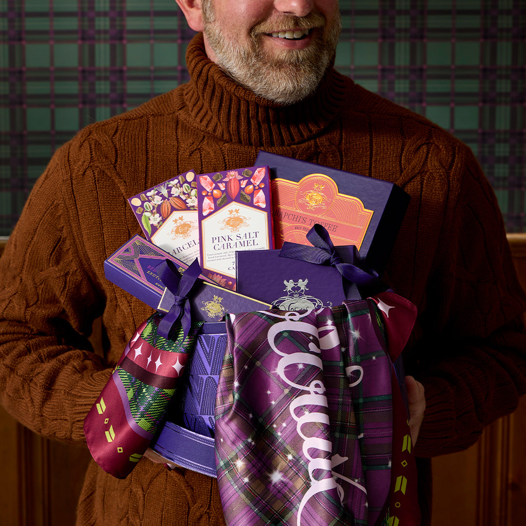 Smiling man in a brown knit turtleneck holding a Best of Vosges Hatbox filled with assorted chocolates