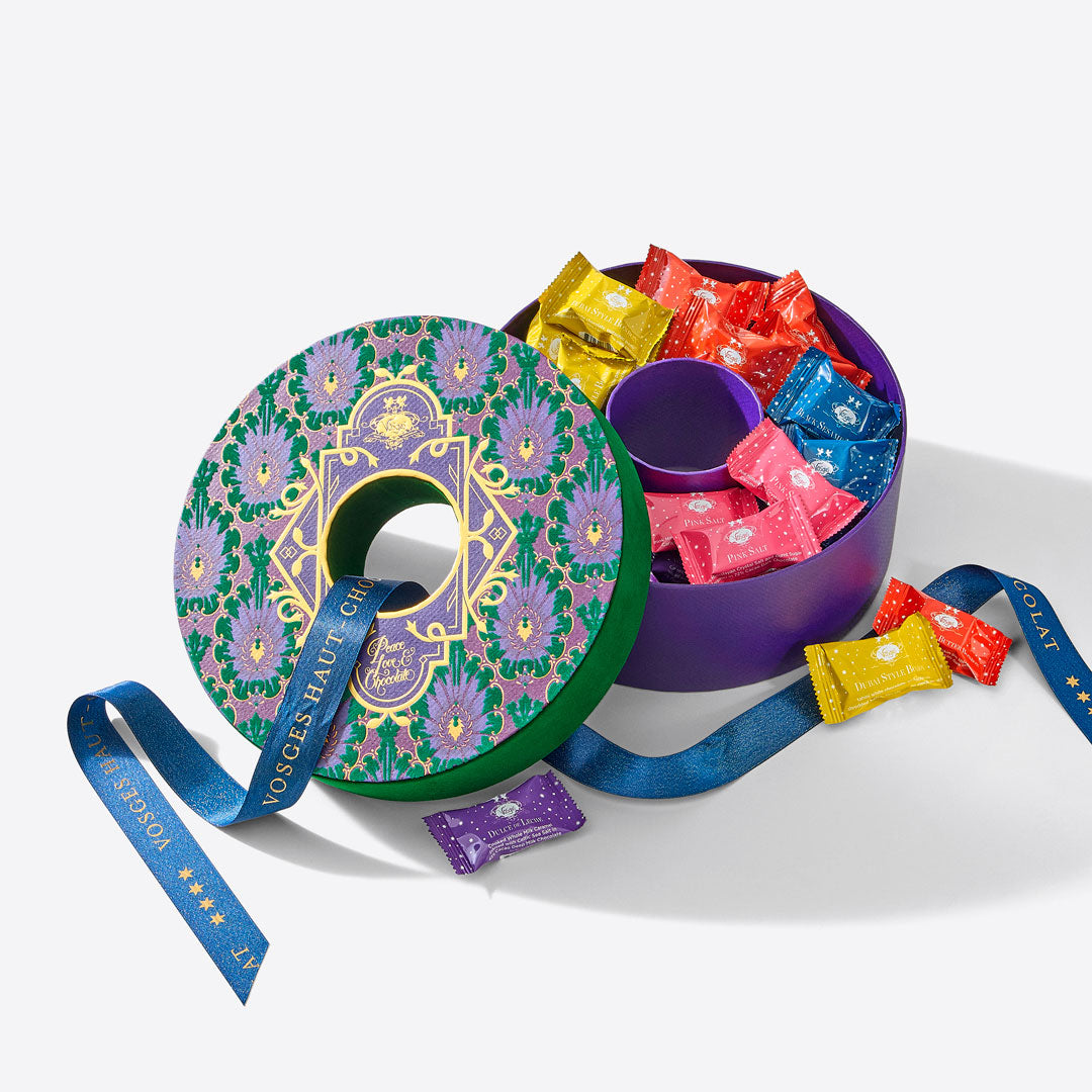 Enchanted Wreath round gift box with a vibrant patterned lid and a purple interior filled with wrapped chocolates.