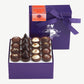 Purple chocolate box embossed with silver foil sits upright displaying four rows of Vosges Italian Truffles on a grey background.  