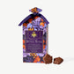 A tall gable box decorated in purple and autumn colored leaves, tied with a purple ribbon stands beside two small chocolate maples leaves on a light grey background.