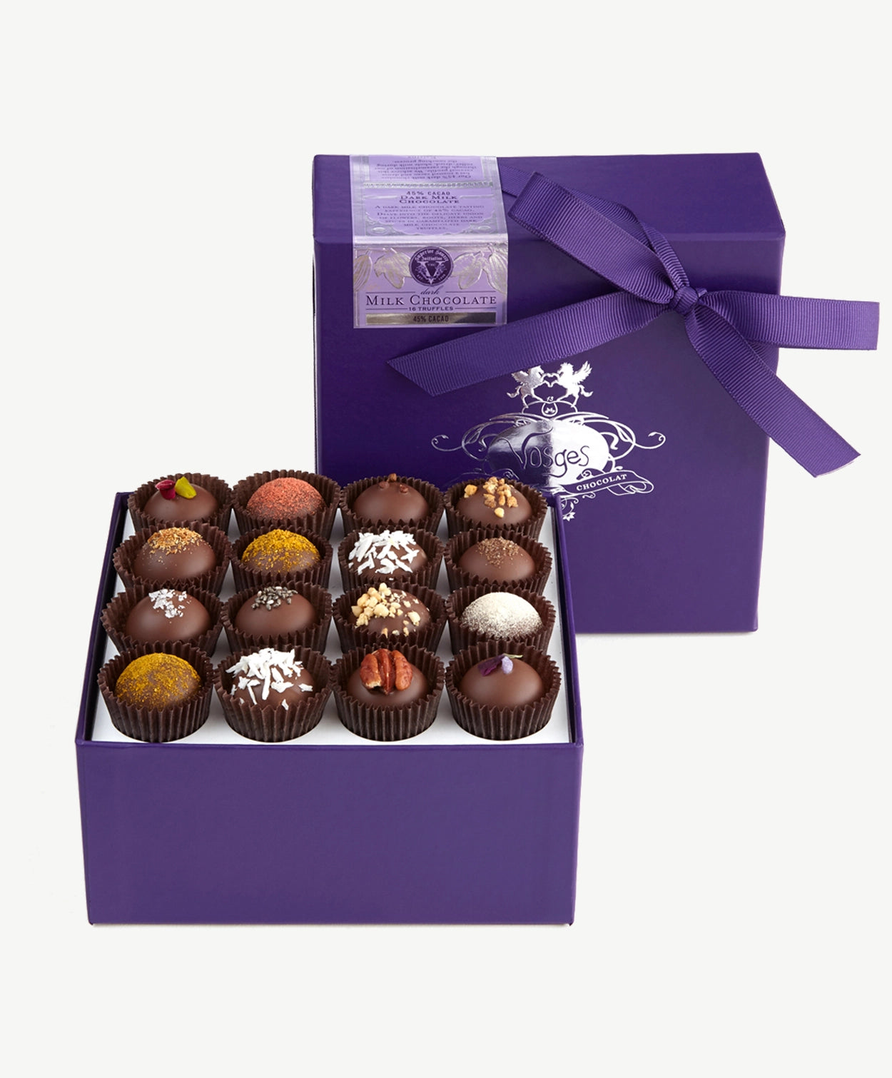 A purple candy box tied with a deep purple ribbon bow sits upright displaying four rows of Vosges milk chocolate truffles topped with toasted curry, sea salt, chopped nuts and spices on a white background.