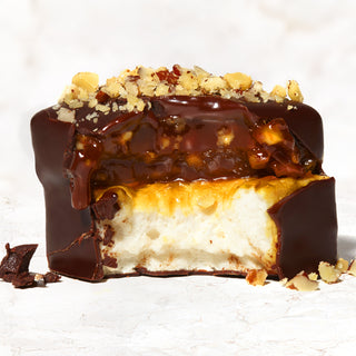 A caramel marshmallow sprinkled with walnut pieces and a bite taken from it on a marble background.