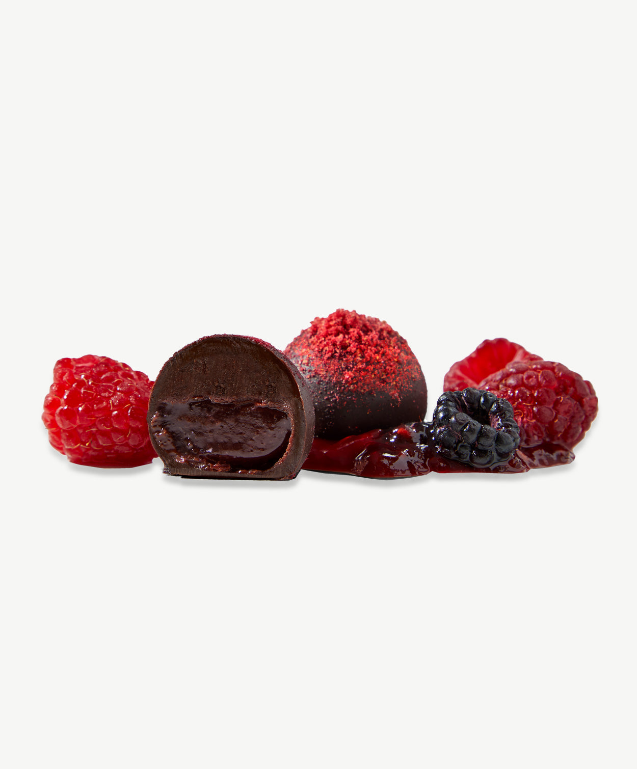 Two Vosges Raspberry Truffles sit beside several fresh black and red raspberries on a light grey background.