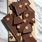Several broken pieces of Vosges Soiree Smash on a wooden cutting board sitting on a marble countertop.  