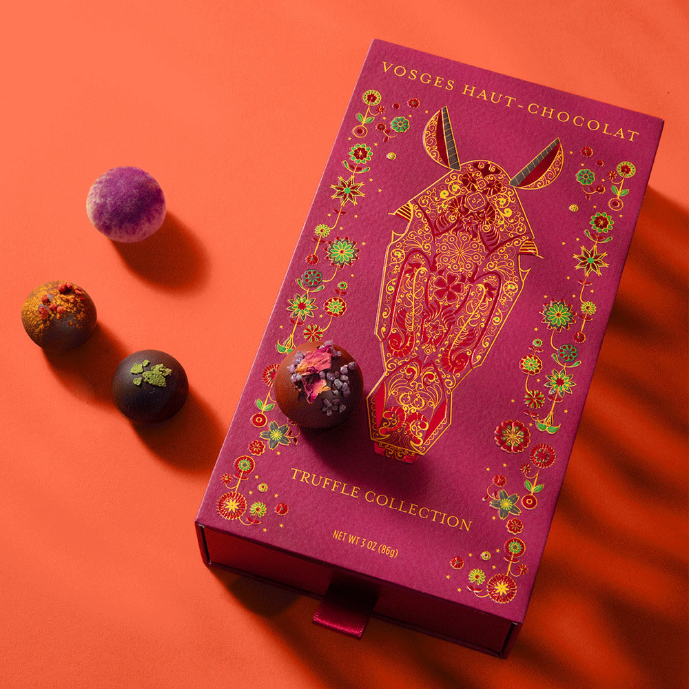 Lunar New Year Truffles purple box on an orange background with three assorted truffles nearby.