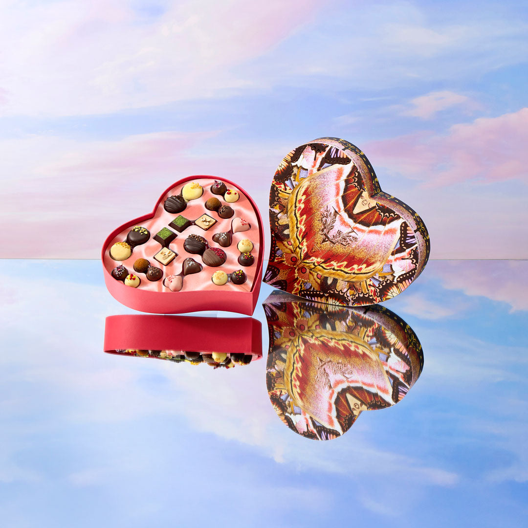 Heart-shaped chocolate box with a reflective surface and sky background
