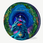 A Vosges chocolate box trimmed in purple velvet, adorned with a large blue dragon and pink egret bird surrounded by green leafy trees infront a swirling dark night sky, sits upright on a light grey background. 