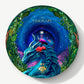 A circular Vosges candy box sits adorned with a wise blue dragon and a pink egret with roses sit in a leafy forest infront a swirling night sky, on a light grey background.