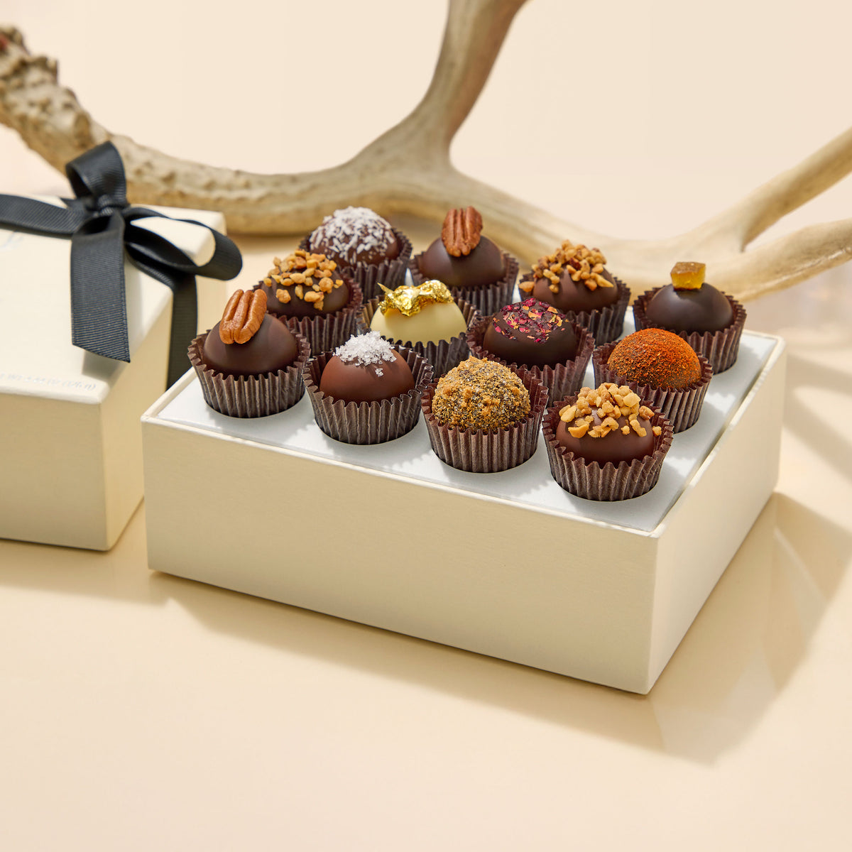 Assorted The Dalmore x Vosges chocolates on a white tray beside a wrapped gift box with a black ribbon