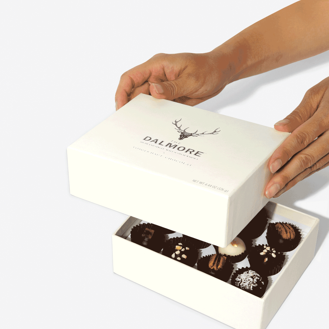 Hands lifting the lid of a white Dalmore Vosges Grand Gift Tower to reveal an assortment of chocolates