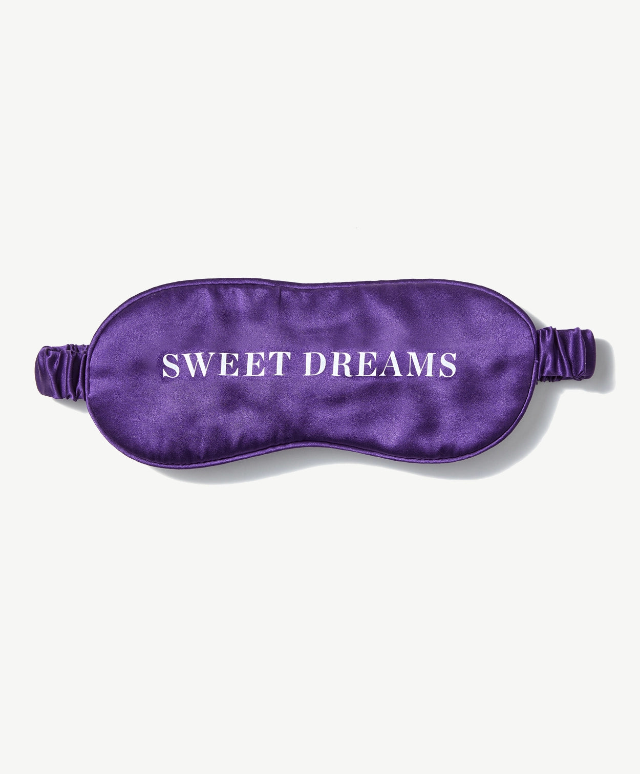 Purple silk sleep mask with elastic band reads, "Sweet Dreams" in white serif font on a light grey background.