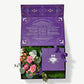 Purple box sits open containing green moss, pink and white flowers tied with a purple ribbon bow and a square Vosges truffle collection on a light grey background.