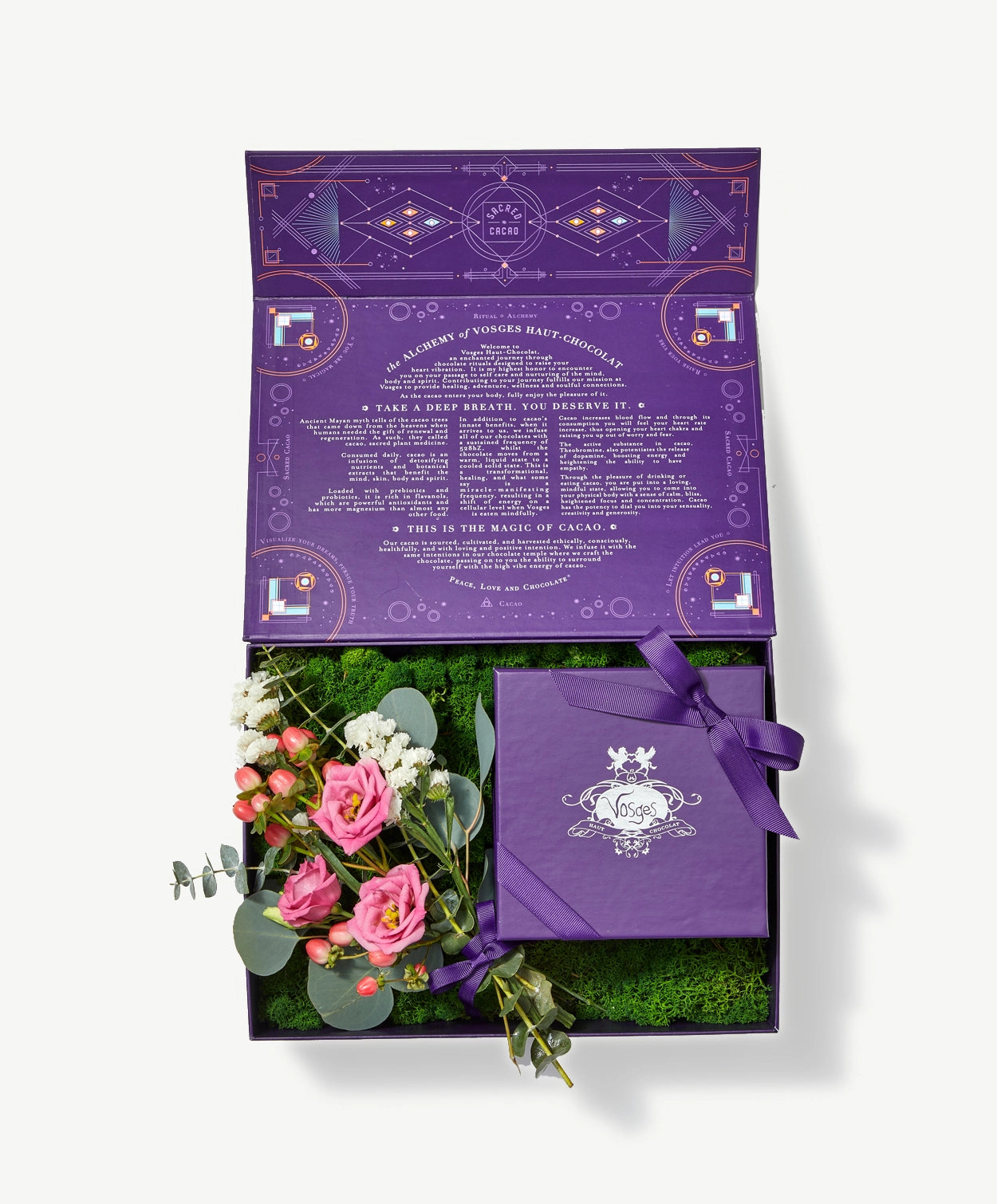 Purple box sits open containing green moss, pink and white flowers tied with a purple ribbon bow and a square Vosges truffle collection on a light grey background.
