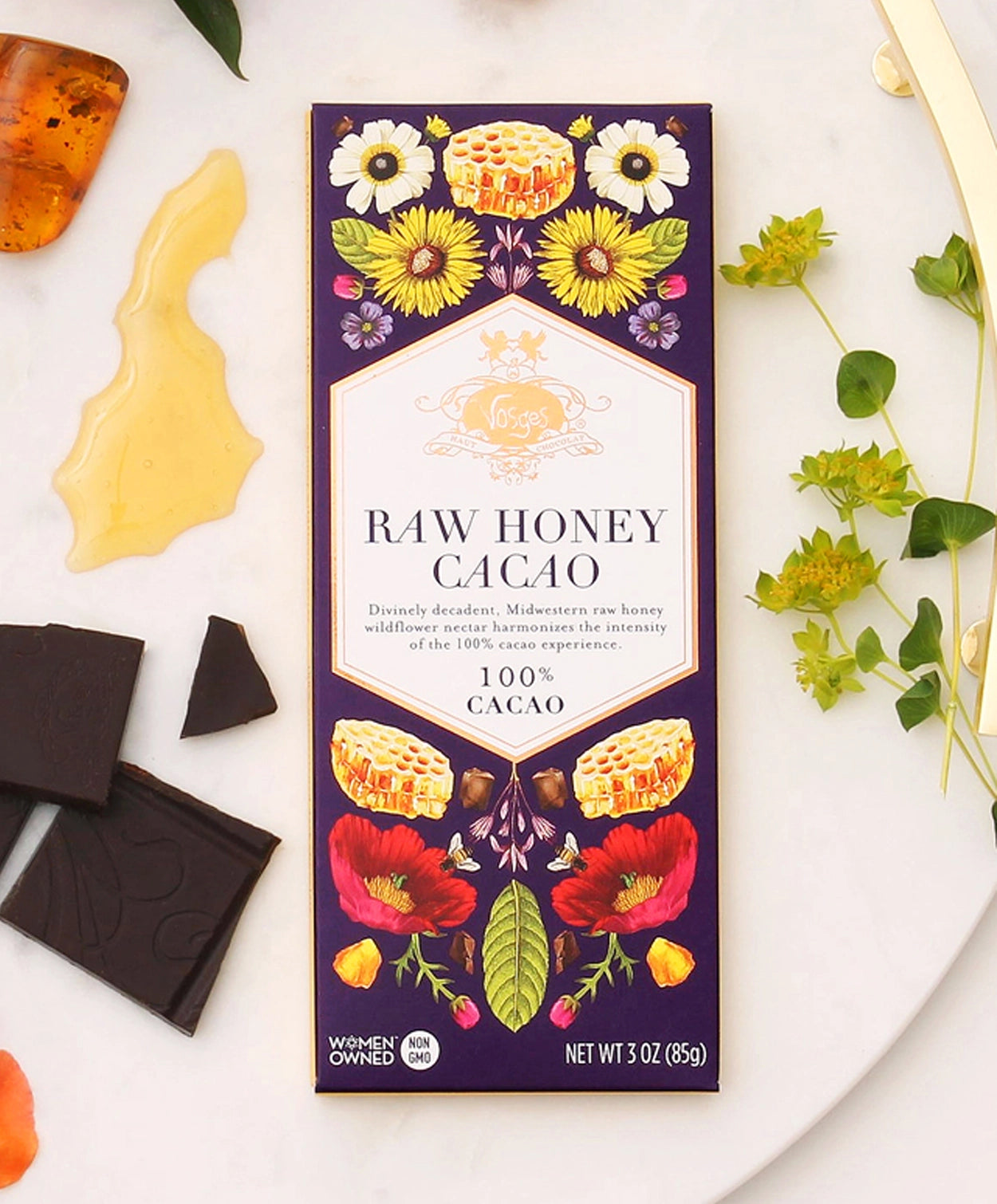 Vosges Raw Honey Cacao bar beside several pieces of chocolate, honey, amber and fresh flowers on a white serving platter.