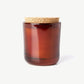 A deeply scented Linnea’s Lights candle in a brown glass jar topped with a natural cork lid sits on a white background.