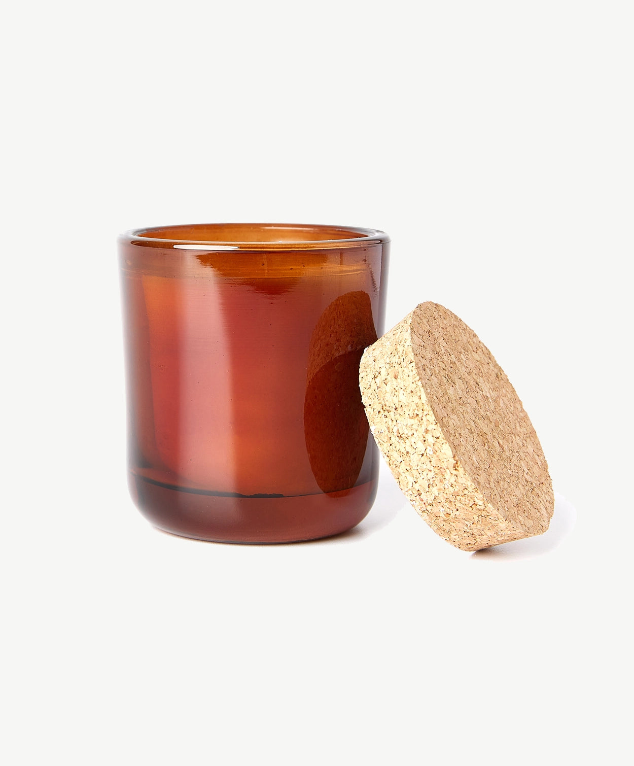 A white Linnea’s Lights scented candle in a brown glass jar with a natural cork wood lid leaning against, on a white background.