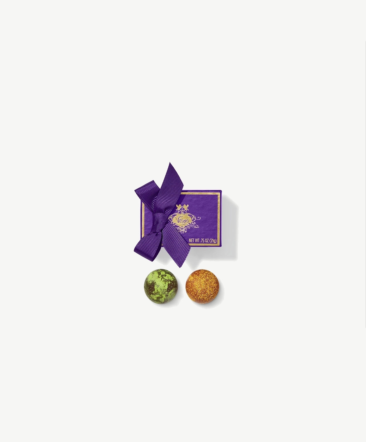A Vosges Naga Truffle and Black Pearl Truffle dusted in toasted curry and green Matcha powder sit side by side in-front a small purple candy box tied with a purple ribbon bow on a grey background.